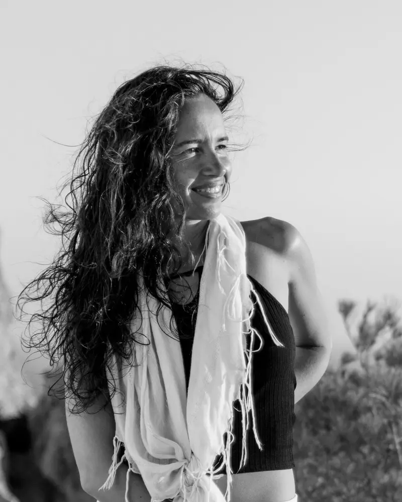 Black-and-white portrait of Dewi Ratna Jewel smiling, her long hair lifted by the wind.