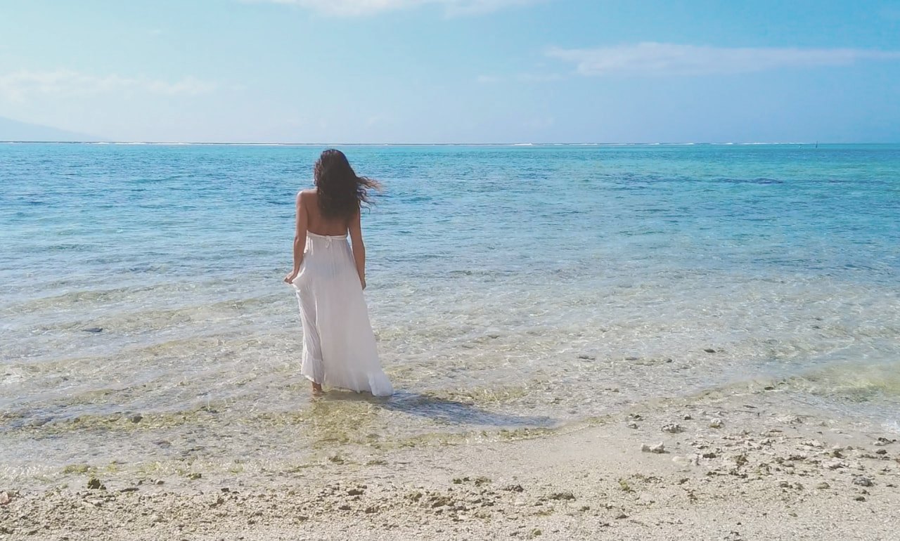 Dewi standing peacefully in shallow sea water wearing a white dress